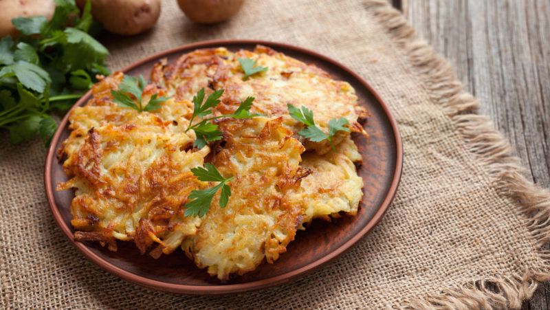 Traditional potato pancakes or latke homemade jewish food Hanukkah celebration recipe. Homemade organic vegan meal in clay dish on vintage wooden background. Rustic style.