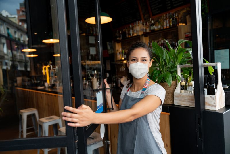 Happy business owner opening the door at a cafe wearing a facemask to avoid the spread of coronavirus - reopening after COVID-19 concepts (Happy business owner opening the door at a cafe wearing a facemask to avoid the spread of coronavirus - reo