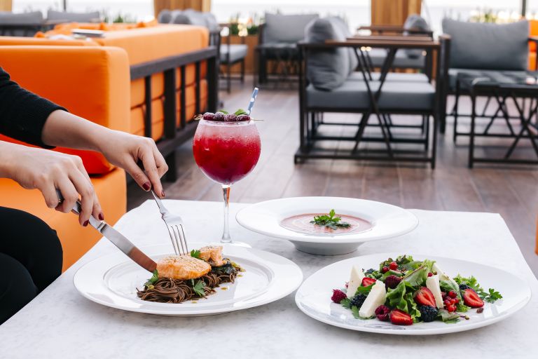 woman having lunch with salmon with brown noodles berry salad soup and cocktail