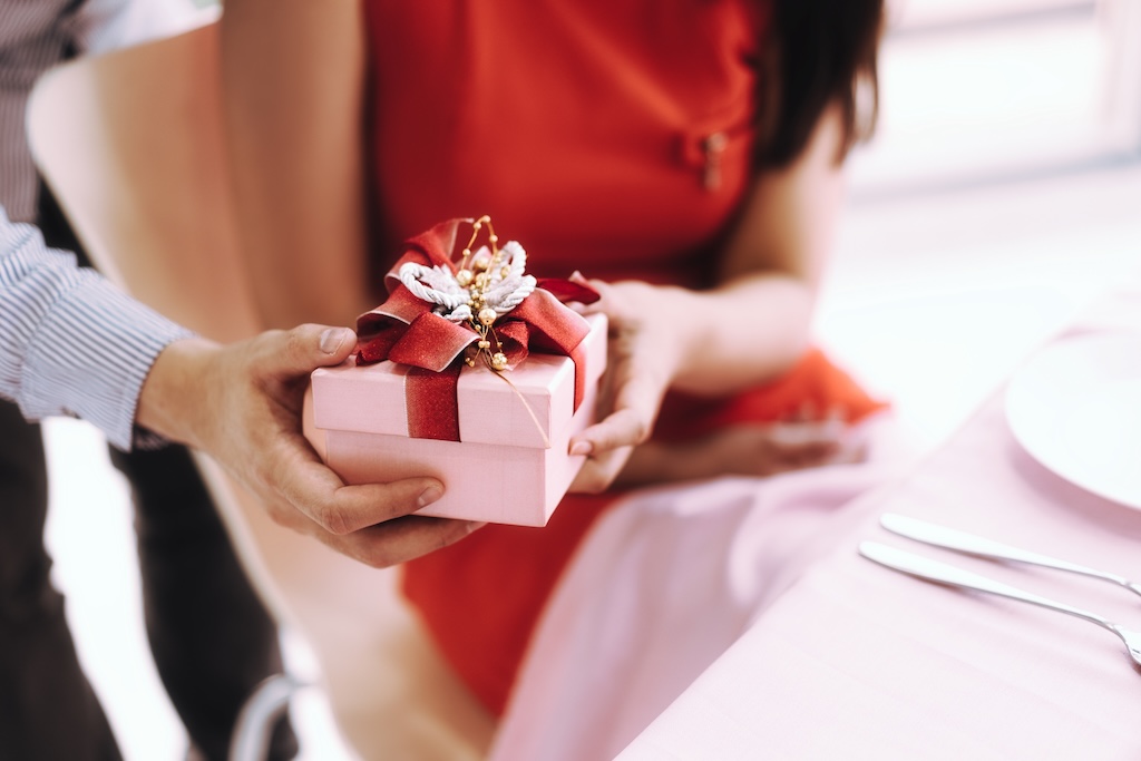 Valentine date at restaurant concept. Couple man and woman with romantic present gift box. At dining table on dinner Background with copy space.